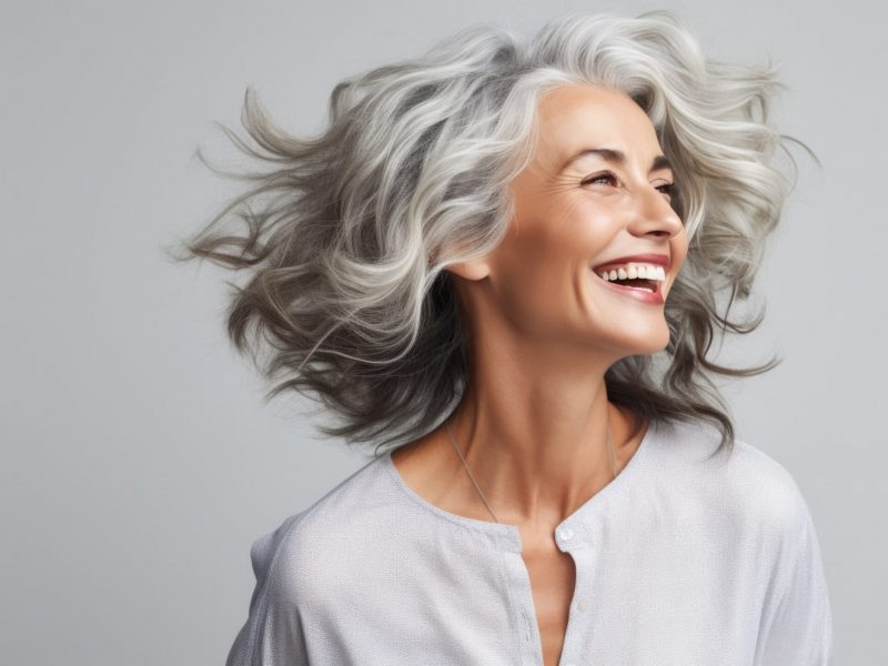 Joyful mature woman with flowing silver hair exudes happiness in a close-up portrait. Her radiant smile highlights her dental health, while her flawless skin